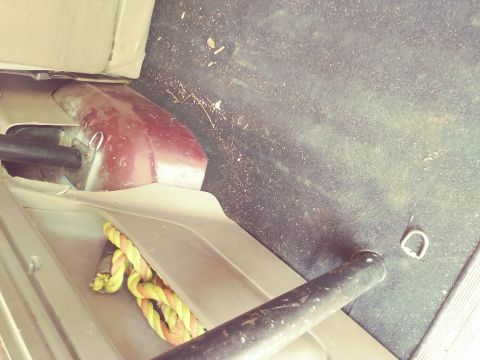 1996 Ford Bronco - The interior of a vehicle shows the rear wheel well area, with a coiled rope and a metal bar visible.