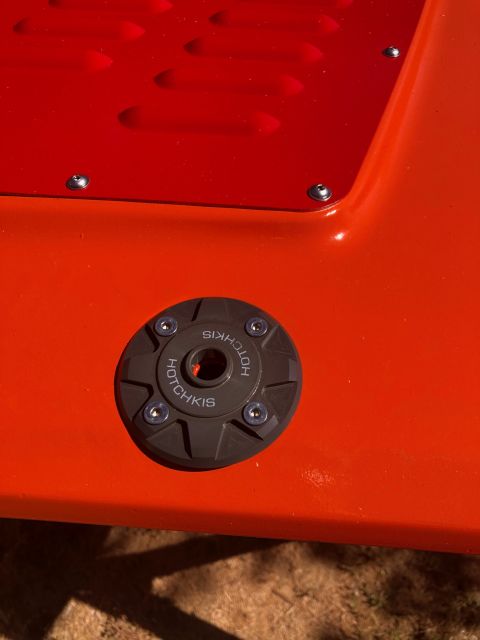1992 Jeep Wrangler - A close-up view of a black Hotchkis brand cap with silver screws attached to an orange vehicle body. The cap has the brand name embossed on…