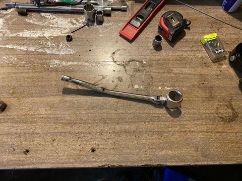 Tools including a socket wrench, sockets, tape measure, and level on a wooden surface.