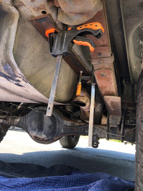 1981 Ford Bronco - Underneath view of a vehicle's rear axle and suspension system, showing leaf springs held in place by clamps and a metal brace. The vehicle…