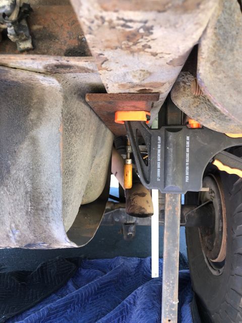 1981 Ford Bronco - A close-up view of the undercarriage of a vehicle, showing rusty metal components and a clamp holding a metal plate in place. A tire and pa…
