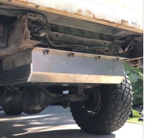 1981 Ford Bronco - The underside of a vehicle shows a custom aluminum fuel tank mounted between the frame rails, above the rear axle and suspension components…