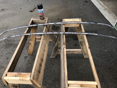 1978 Ford Bronco - Two curved chrome trim pieces are laid out on a wooden sawhorse structure outdoors. A can of spray paint sits on top of the sawhorse to the…