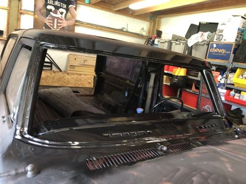 1978 Ford Bronco - The interior of a black classic pickup truck is shown from a front 3/4 angle, focusing on the windshield area and dashboard. The truck appe…