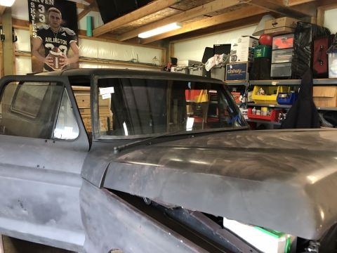 1978 Ford Bronco - A close-up, low-angle view of the front driver's side of a dark-colored, classic Ford Bronco undergoing restoration. The vehicle is in a ga…