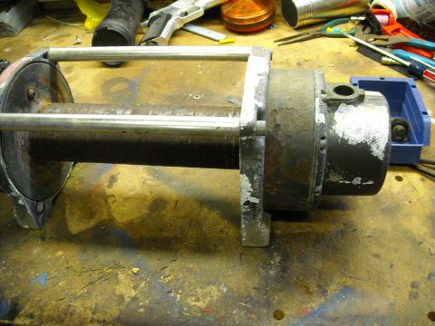 1992 Jeep Wrangler - A close-up shot shows a rusty motor and metal rod assembly mounted on a workbench. Various tools and other workshop items are visible in th…