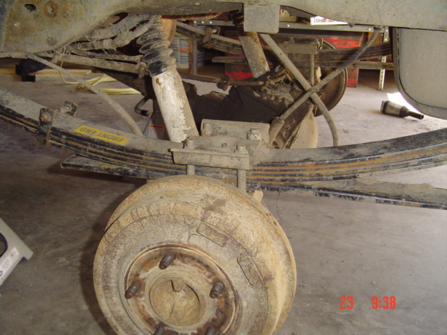 Close-up of a vehicle's rear suspension with leaf springs, shock absorber, and brake drum. A yellow sticker reads 'FRONT END'