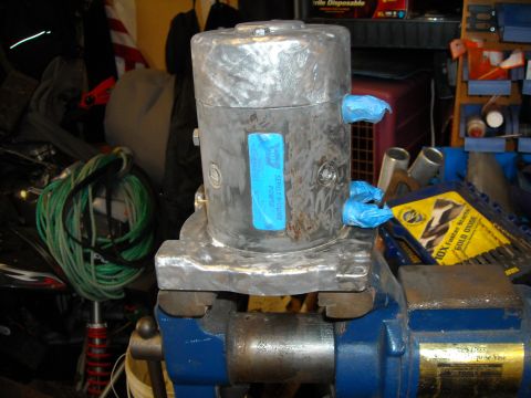 1992 Jeep Wrangler - A metal motor is clamped in a blue vise. The motor has blue tape covering two small openings and a blue label with white text.