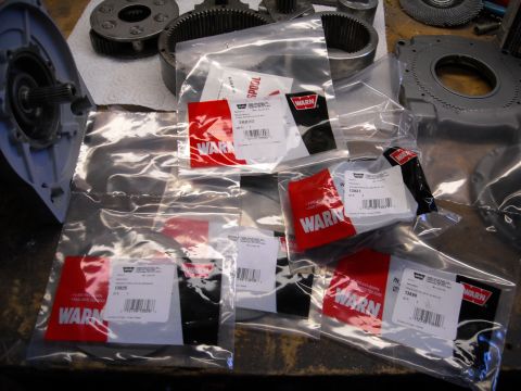 1992 Jeep Wrangler - Several sealed plastic bags containing Warn winch parts are laid out on a workbench next to a disassembled winch housing and gears.