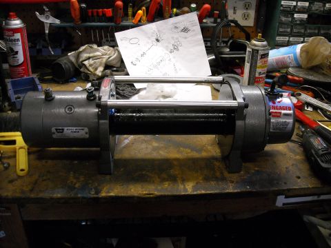 1992 Jeep Wrangler - A gray electric winch with a black drum is mounted on a workbench surrounded by tools and supplies. A label on the winch reads "WARN MB8000…