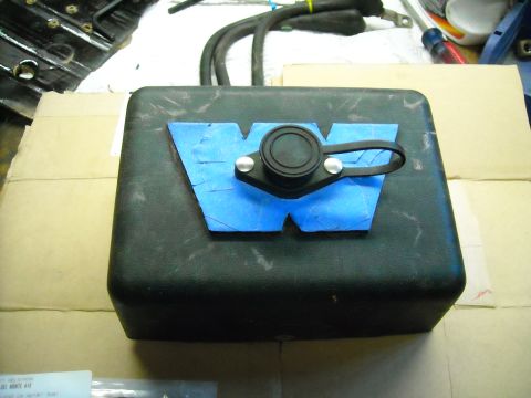 1992 Jeep Wrangler - A black, rectangular electronic module with a blue "W" logo taped to the top. The module has a black circular cap with a loop attached to i…