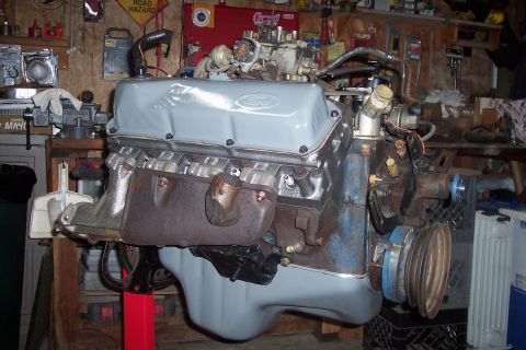 1978 Ford Bronco - A Ford V8 engine, painted light gray, is mounted on a red engine stand in a workshop. The engine features a carburetor, exhaust manifolds,…