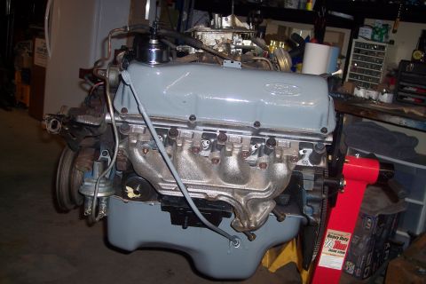 1978 Ford Bronco - A Ford V8 engine, painted gray, is mounted on a red engine stand in a workshop. The engine features a carburetor, exhaust manifolds, and an…