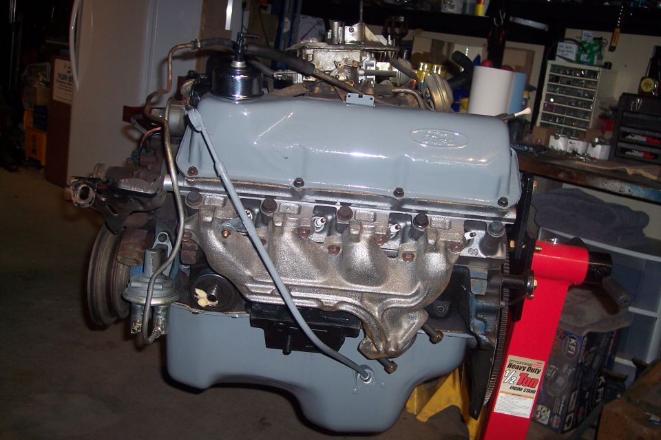 Gray Ford V8 engine on a red engine stand in a workshop.