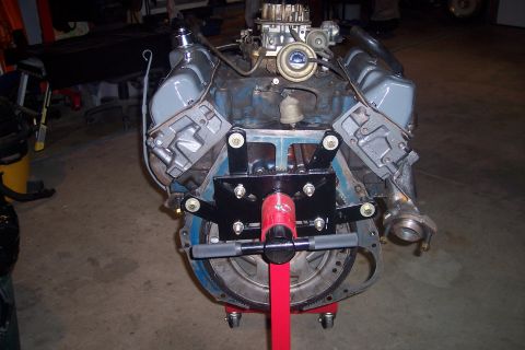 1978 Ford Bronco - A V8 engine is mounted on a red engine stand. The engine has a carburetor and is painted blue with gray valve covers.