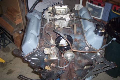 1978 Ford Bronco - A close-up view of a V8 engine block with gray painted valve covers and a carburetor. The engine appears to be partially assembled or under…