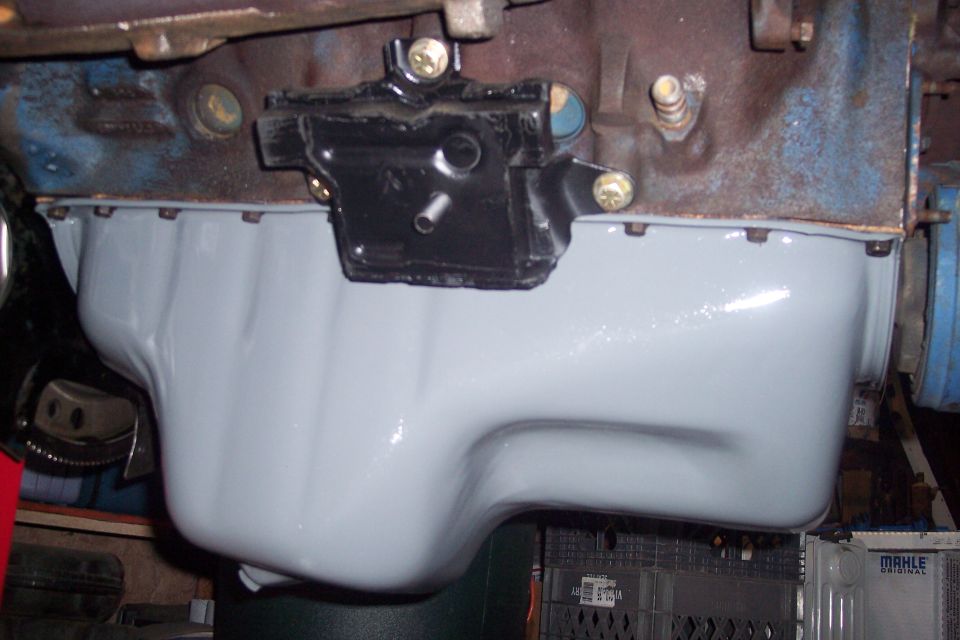 Newly painted light gray oil pan installed on a Ford V8 engine block with a black bracket attached.