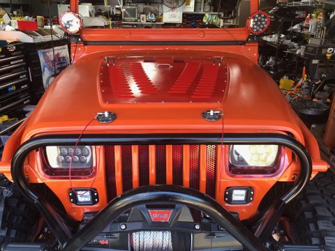 1992 Jeep Wrangler - The front view of an orange Jeep Wrangler with a black grille guard and a winch mounted below. It features aftermarket LED headlights and a…