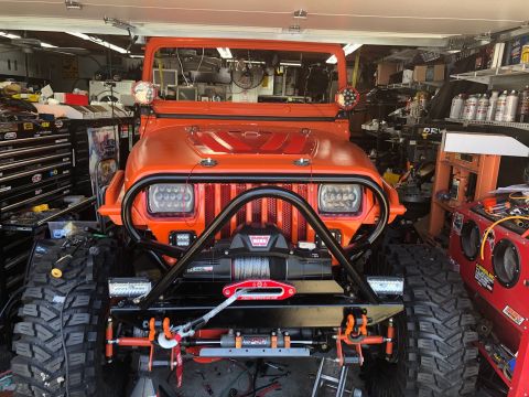 1992 Jeep Wrangler - Front view of an orange Jeep Wrangler parked in a cluttered garage. The vehicle has been heavily modified with large off-road tires, a winc…