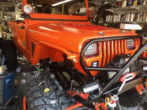 1992 Jeep Wrangler - An orange Jeep Wrangler is shown in a garage with its hood open, revealing a custom grille and winch. The vehicle is heavily modified with…