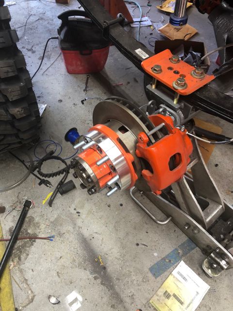 1992 Jeep Wrangler - A close-up view of a vehicle's front brake assembly, featuring an orange brake caliper and a silver hub spacer, is shown in a workshop sett…