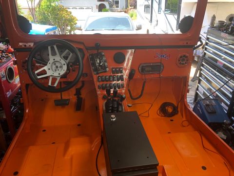 1992 Jeep Wrangler - The interior of an orange Jeep Wrangler shows a custom dashboard with multiple switches, a steering wheel, and floor pedals. The vehicle ap…