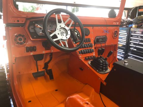 1992 Jeep Wrangler - The interior of an orange Jeep Wrangler shows a custom dashboard with a silver steering wheel, multiple toggle switches, and gear shifters.…