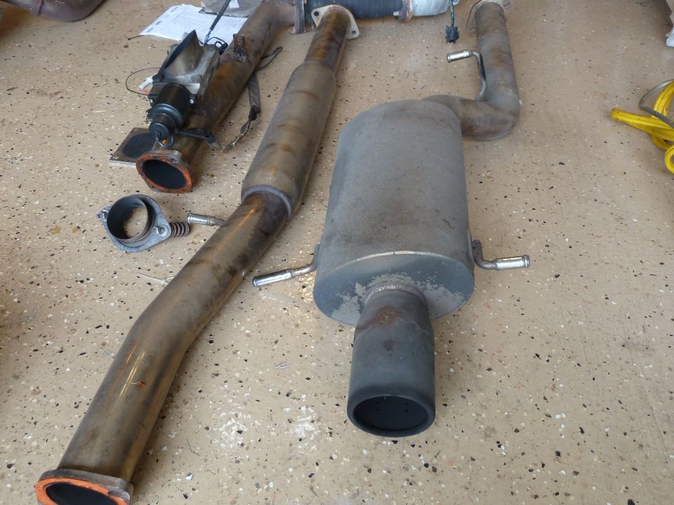Subaru Impreza exhaust system parts on a speckled floor.