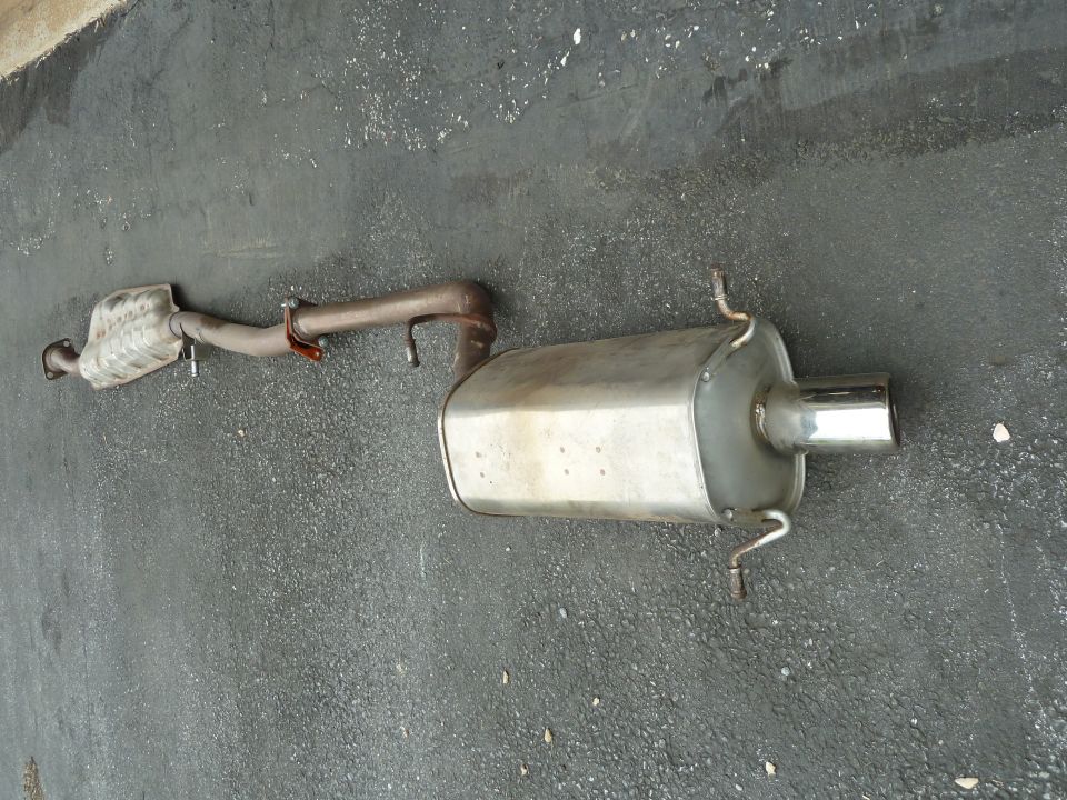 Exhaust system with muffler and catalytic converter on asphalt.