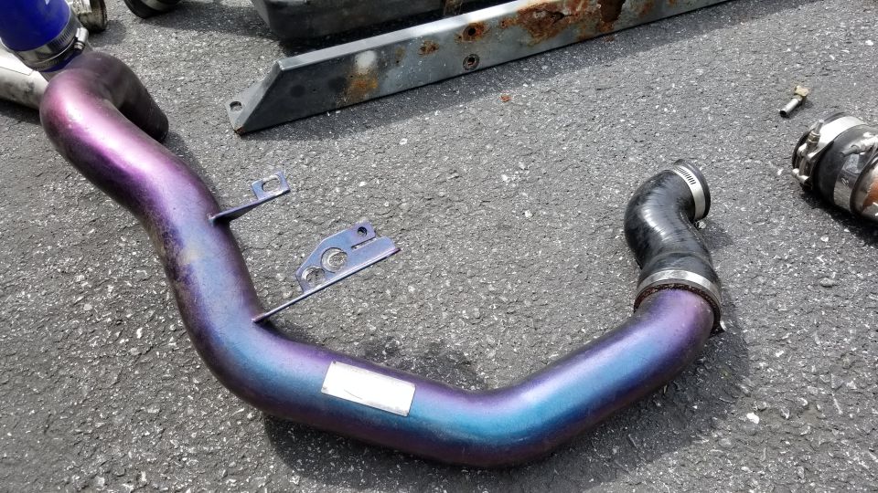Custom metallic purple and blue exhaust pipe with mounting brackets on asphalt.