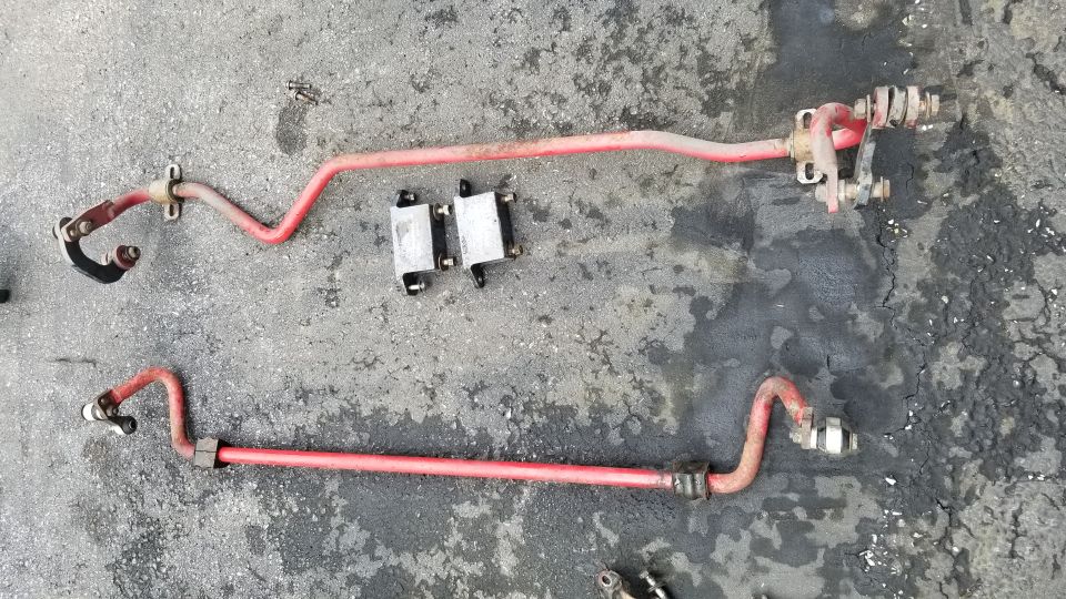Two red sway bars and two metal blocks on asphalt.