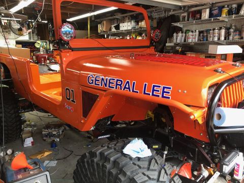1992 Jeep Wrangler - An orange Jeep Wrangler is parked in a garage, with the words "GENERAL LEE" and the number "01" visible on its side. The vehicle appears to…