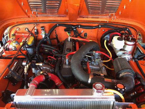 1992 Jeep Wrangler - A detailed, close-up view of the engine bay of an orange Jeep Wrangler, showcasing various aftermarket modifications and components.