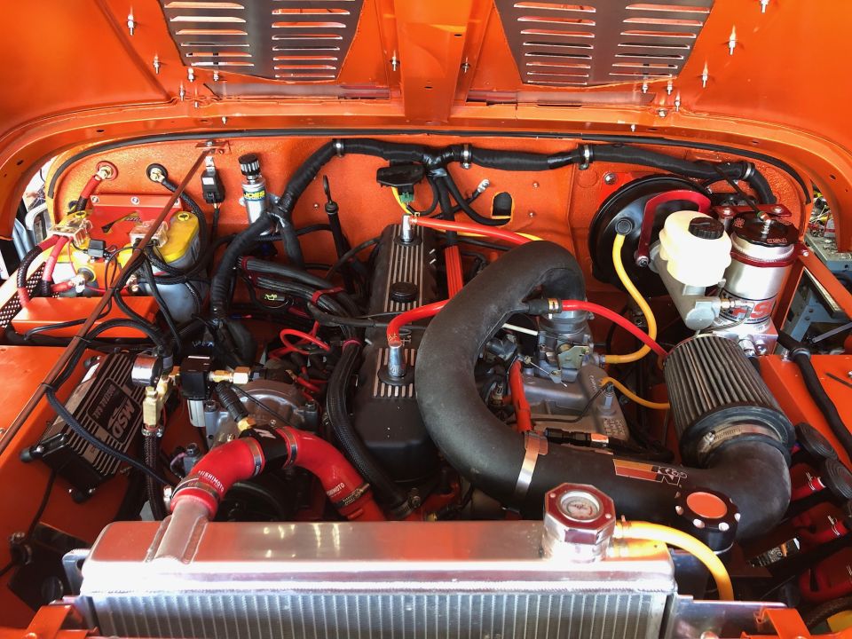 Close-up of an orange Jeep Wrangler engine bay with custom parts and wiring.