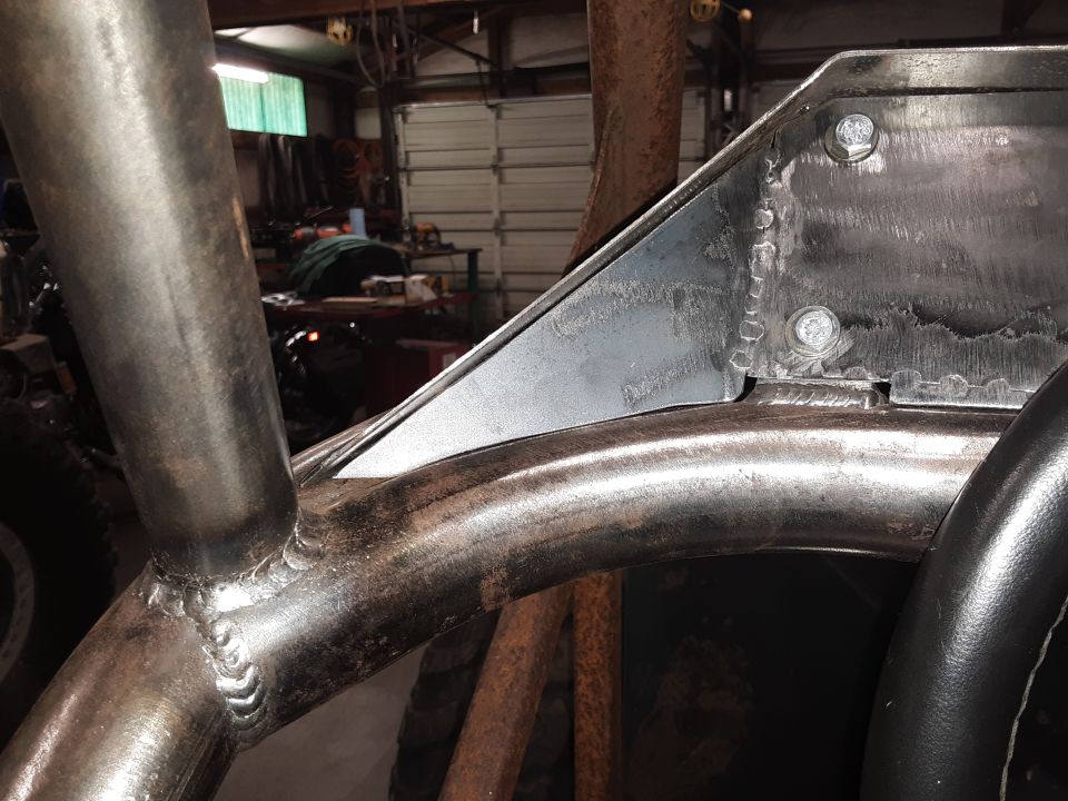 Close-up of a welded metal roll cage inside a vehicle, workshop in background.
