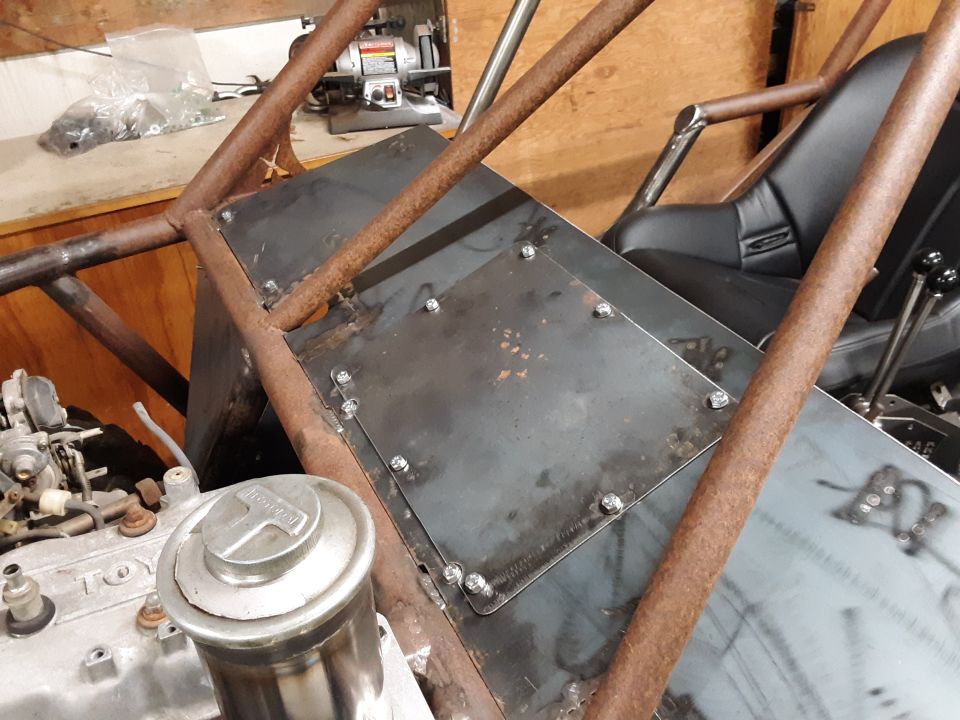 Custom metal plate bolted to rusty frame with Toyota engine and black racing seat visible.