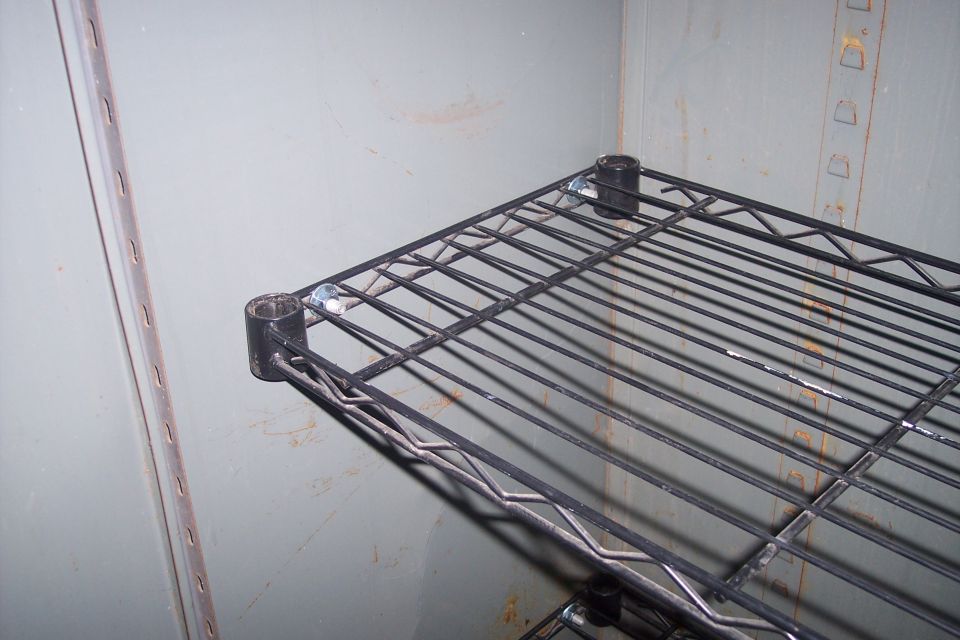 Black wire shelf unit with silver bolts against a grey textured wall.