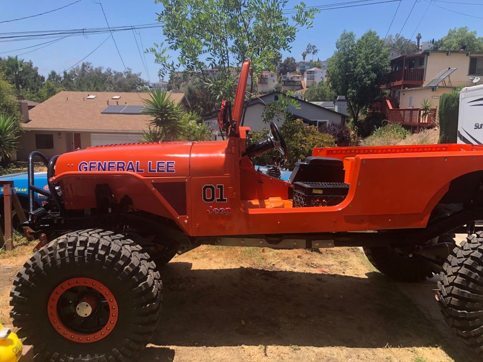 Modified orange Jeep Wrangler "General Lee" with large tires and "01" on the side.