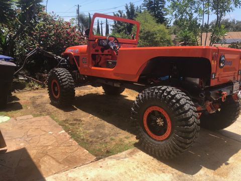 1992 Jeep Wrangler - A custom-built, bright orange Jeep Wrangler with large off-road tires and a roll cage is parked on a paved driveway. The vehicle has "GENER…