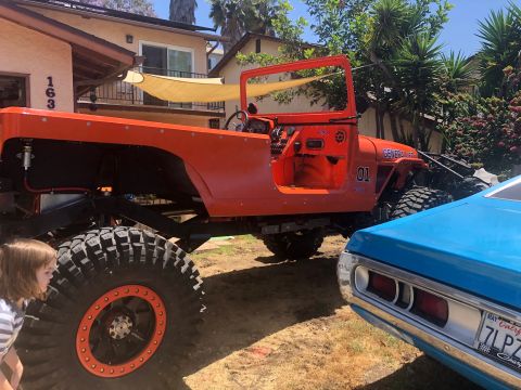 1992 Jeep Wrangler - A bright orange, modified Jeep Wrangler is parked outdoors next to a blue car. The Jeep has large off-road tires and visible modifications…