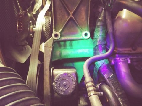 1996 Ford Bronco - Close-up view of a vehicle's engine bay, focusing on the power steering reservoir and various hoses and belts. The green-painted metal brac…