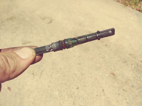 1996 Ford Bronco - A hand holds a dark colored dipstick with a mesh filter and green residue at the end. The dipstick appears to be coated in oil and grime.