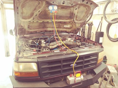 1996 Ford Bronco - The engine bay of a maroon Ford Bronco is open, with a manifold gauge set and vacuum pump connected to the AC system. The vehicle is in a g…