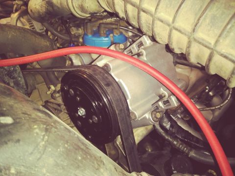 1996 Ford Bronco - A close-up view of the engine bay of a 1996 Ford Bronco, focusing on the air conditioning compressor and serpentine belt.