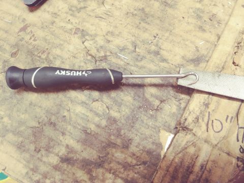 1996 Ford Bronco - A close-up shot of a Husky brand file tool with a black handle and a metal file end, resting on a textured wooden surface. The tool is posi…