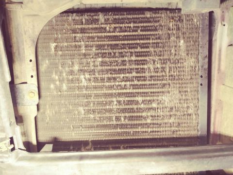 1996 Ford Bronco - A close-up view of a dirty and corroded radiator or condenser unit, likely from a 1996 Ford Bronco, showing bent fins and debris.