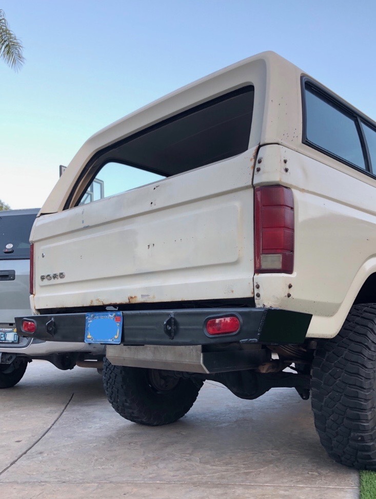 Rear driver's side of a white 1980s Ford Bronco with custom bumper and off-road tires.