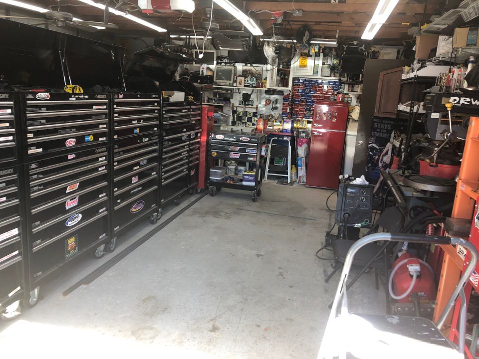 Cluttered garage scene with toolboxes, red refrigerator, and equipment.