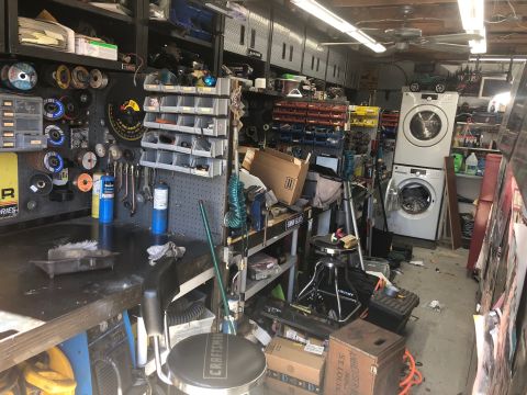 1992 Jeep Wrangler - This is a cluttered garage scene with various tools, storage bins, and appliances. A workbench is visible in the foreground with a stool an…