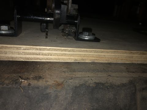 1980 Ford Bronco - A close-up view shows a metal bracket with a bolt and washer attached to a plywood surface. The plywood is layered and sits above a dark, t…
